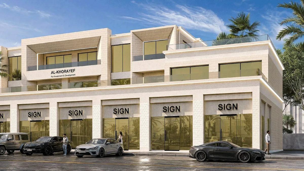 The commercial building by day, a run of glazed shopfronts with signage zones under a clean office mass.